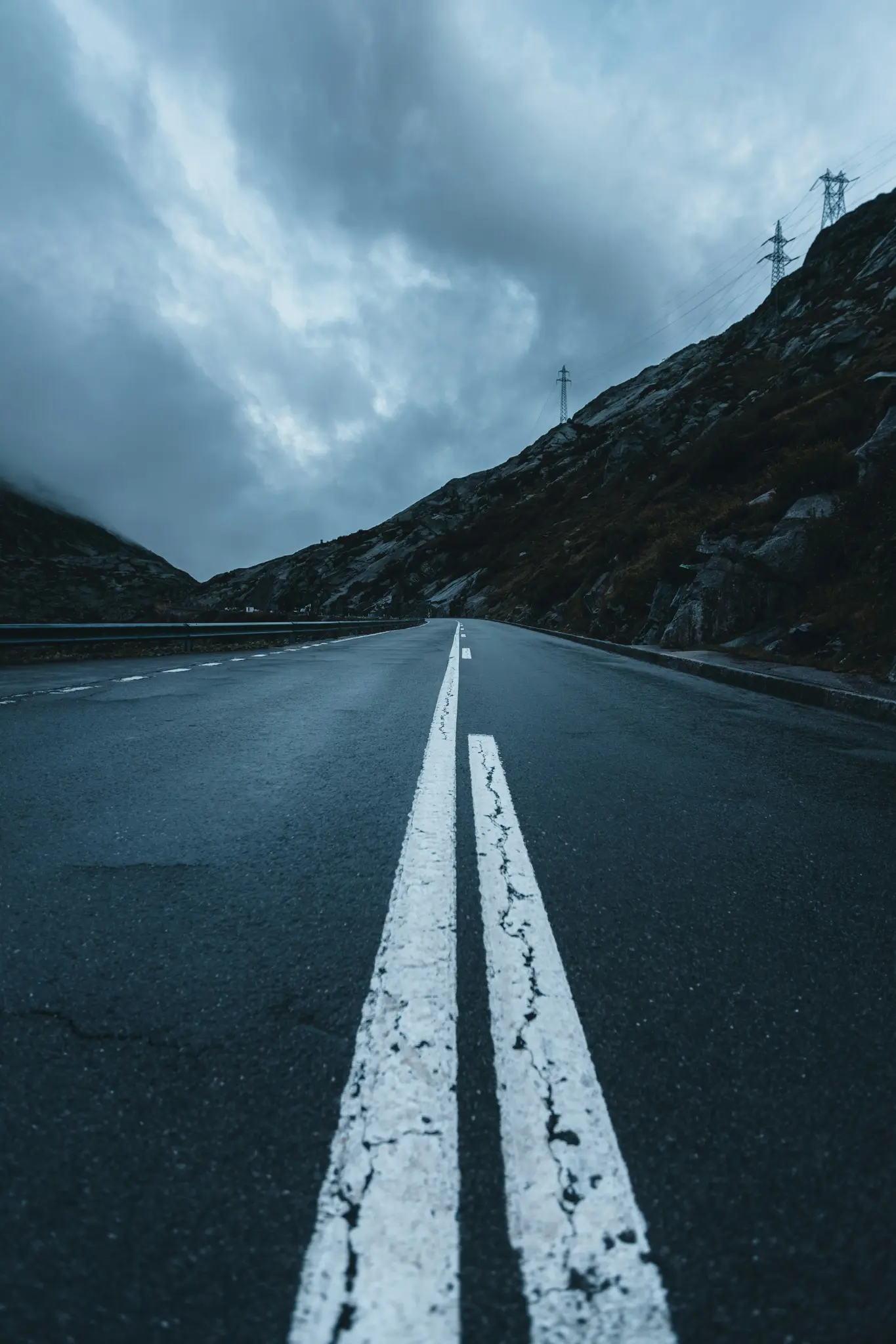 Una vista en ángulo bajo de una carretera de asfalto oscura con prominentes líneas blancas dobles, que se curva hacia una