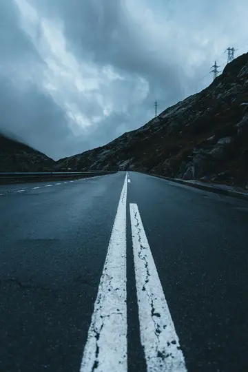 Eine Aufnahme aus niedriger Perspektive einer dunklen Asphaltstraße mit ausgeprägten doppelten weißen Linien, die sich in