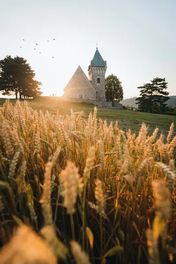 Eine Steinkirche mit einem grün bedachten Turm auf einem grasbewachsenen Hügel, gebadet im Licht der goldenen Stunde, mit
