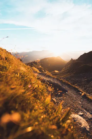 Un vibrante paisaje de montaña al atardecer, con un sinuoso camino de tierra a través de laderas cubiertas de hierba y picos