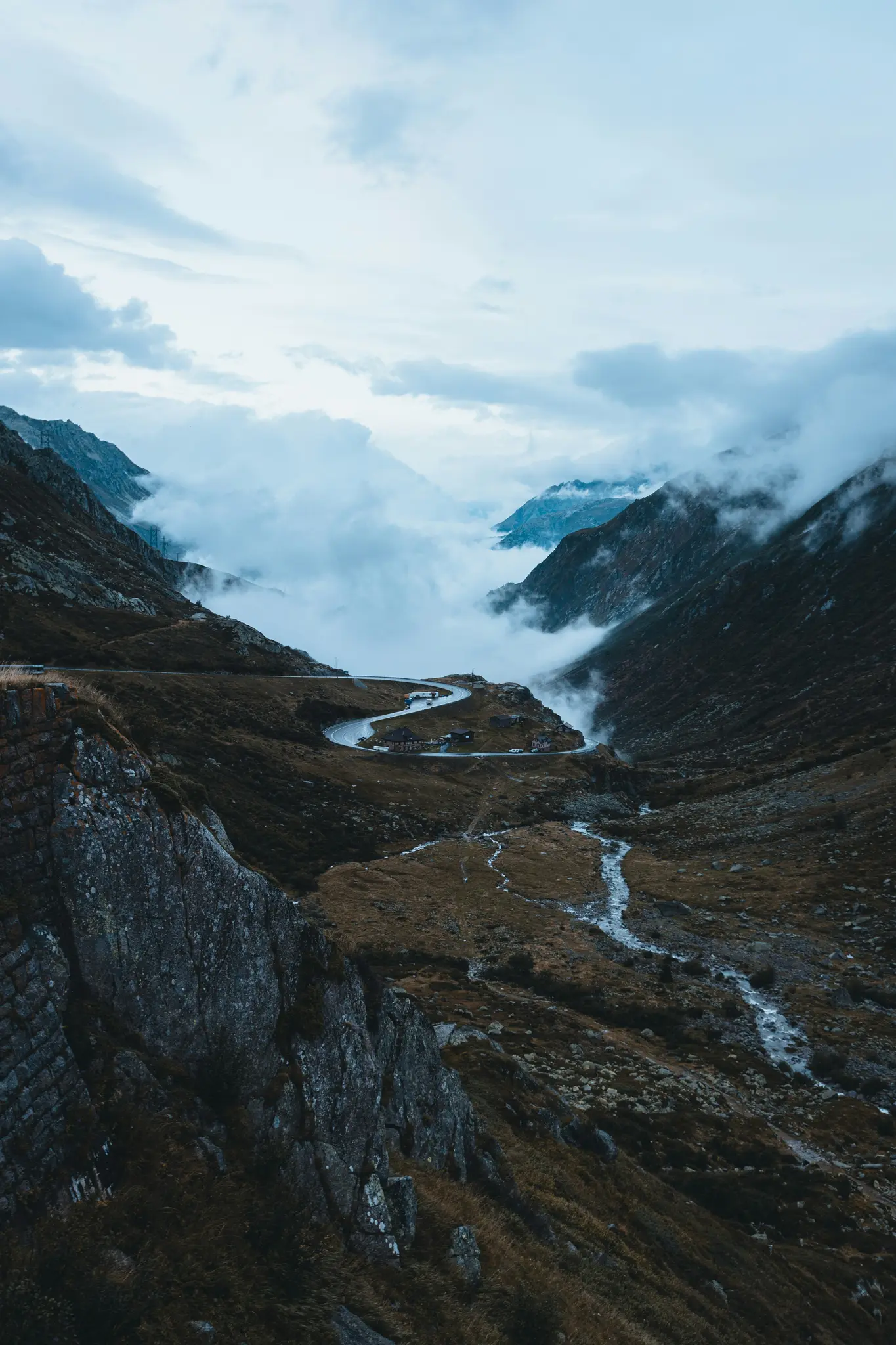 Eine Luftaufnahme einer kurvenreichen Bergstraße, die sich durch ein Tal schlängelt, teilweise umhüllt von tief hängenden