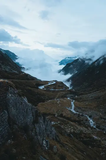 Eine Luftaufnahme einer kurvenreichen Bergstraße, die sich durch ein Tal schlängelt, teilweise umhüllt von tief hängenden
