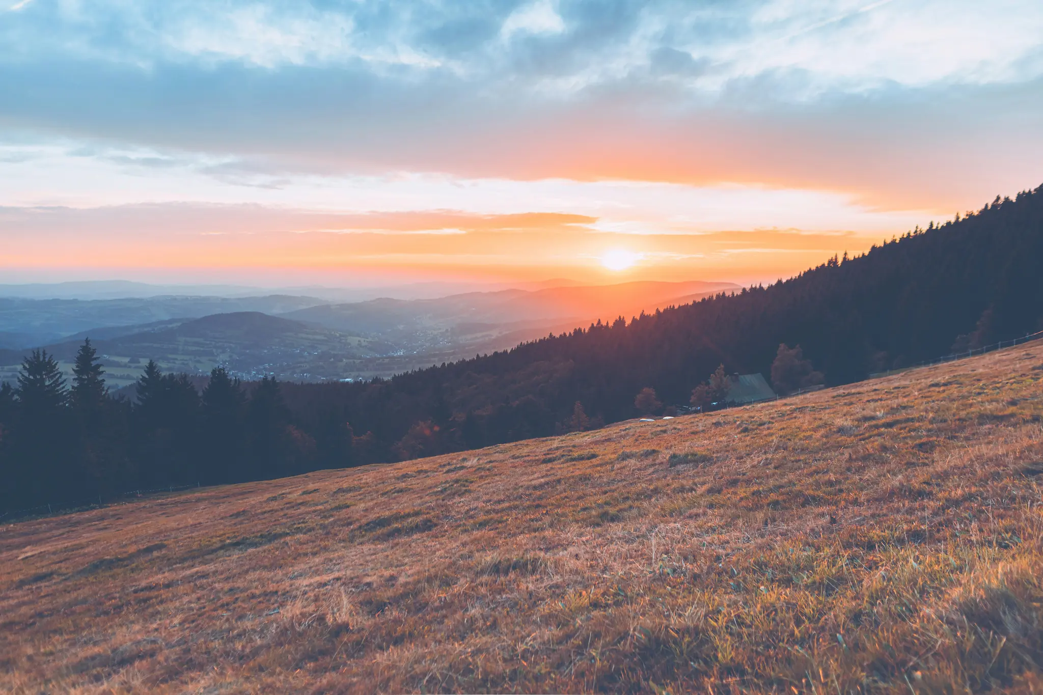 Ein lebendiger Sonnenuntergang über einer weiten Berglandschaft. Der Vordergrund zeigt einen sonnenbeschienenen