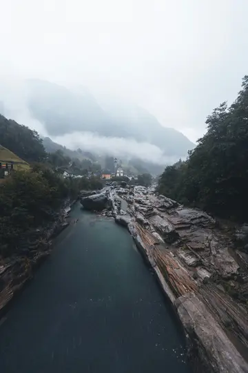 Un río azul oscuro fluye a través de un desfiladero con formaciones rocosas en capas. Un pueblo con el campanario de una
