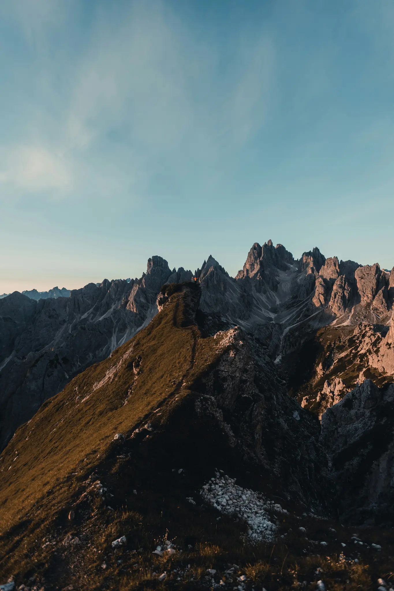 Eine weite Landschaftsaufnahme einer Bergkette während der goldenen Stunde. Ein grasbewachsener Kamm führt zu zerklüfteten