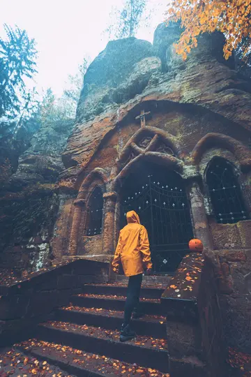 Una persona con un impermeable amarillo brillante camina por escalones de piedra cubiertos de hojas de otoño hacia una