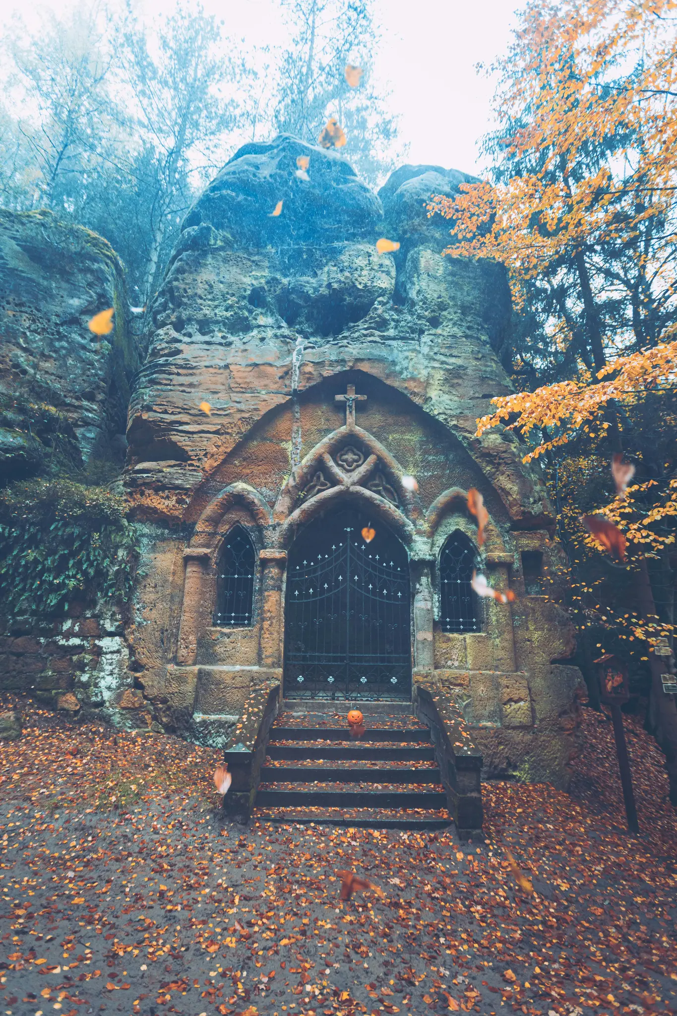 Eine Steinkapelle, die in eine große Felswand gehauen wurde, mit einem dunklen, verzierten Tor und einer Treppe, die mit