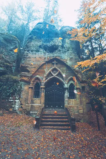Eine Steinkapelle, die in eine große Felswand gehauen wurde, mit einem dunklen, verzierten Tor und einer Treppe, die mit