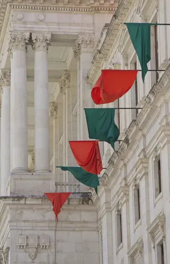 Una magnifica facciata in pietra chiara con colonne classiche e intagli ornati. Banner rossi e verdi pendono da…