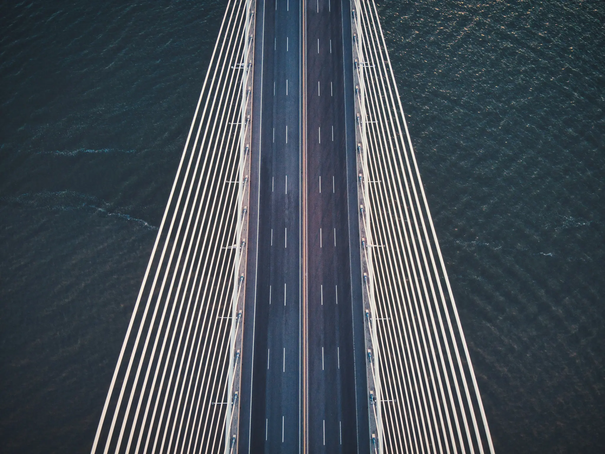 Una vista aérea, de arriba abajo, de un moderno puente atirantado. La carretera de asfalto oscura tiene marcas de carril