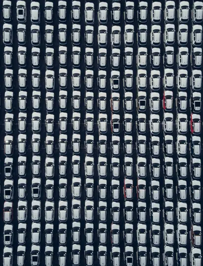 Una toma aérea de un vasto aparcamiento lleno de cientos de coches blancos nuevos, cuidadosamente dispuestos en filas largas