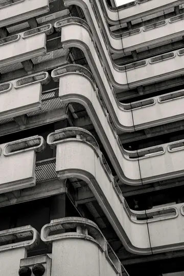 Ein Schwarz-Weiß-Foto, das die geschwungenen Betonbalkone und gitterartigen Gehwege eines brutalistischen Gebäudes von unten