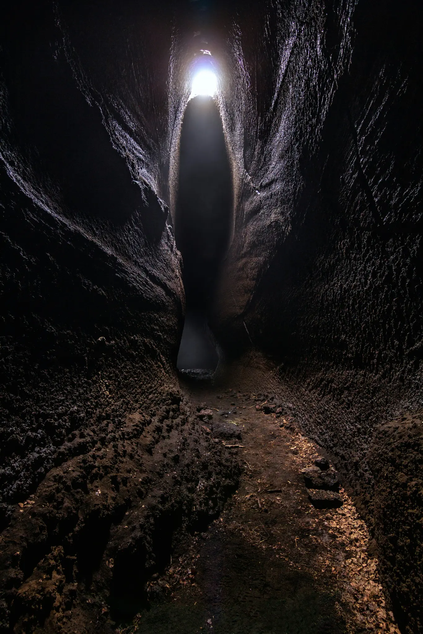En vertikal bild som tittar ner i en mycket smal, mörk grottpassage mot ett klart, cirkulärt ljus i slutet.