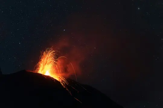 Et dramatisk nattebillede af et vulkanudbrud, der spyder klart orange og rødt lava og gnister ud i den mørke, stjernefyldte