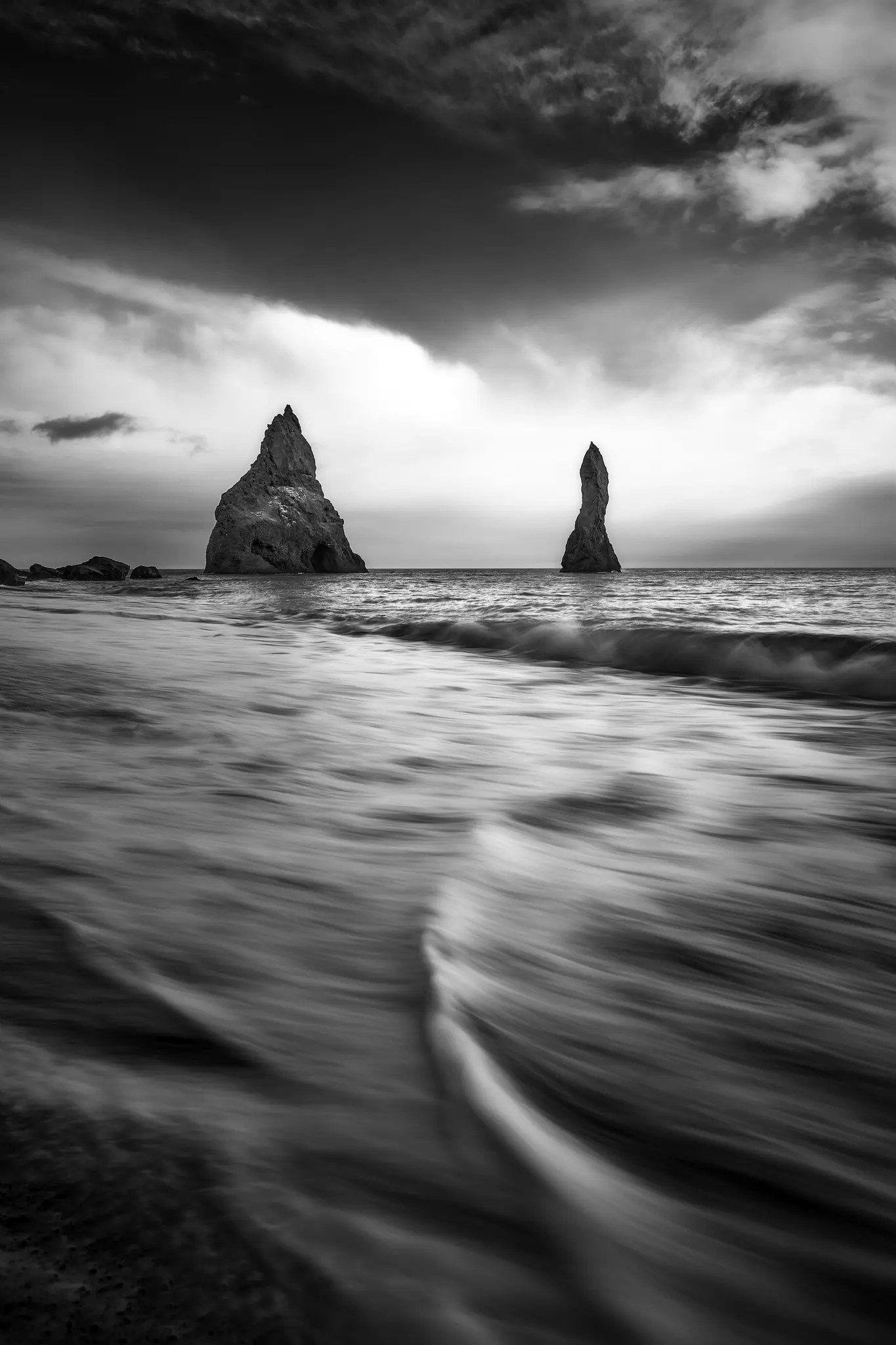 Černobílá fotografie dramatické mořské krajiny s dlouhou expozicí. Dva vysoké, zubaté mořské pilíře se tyčí z oceánu pod…