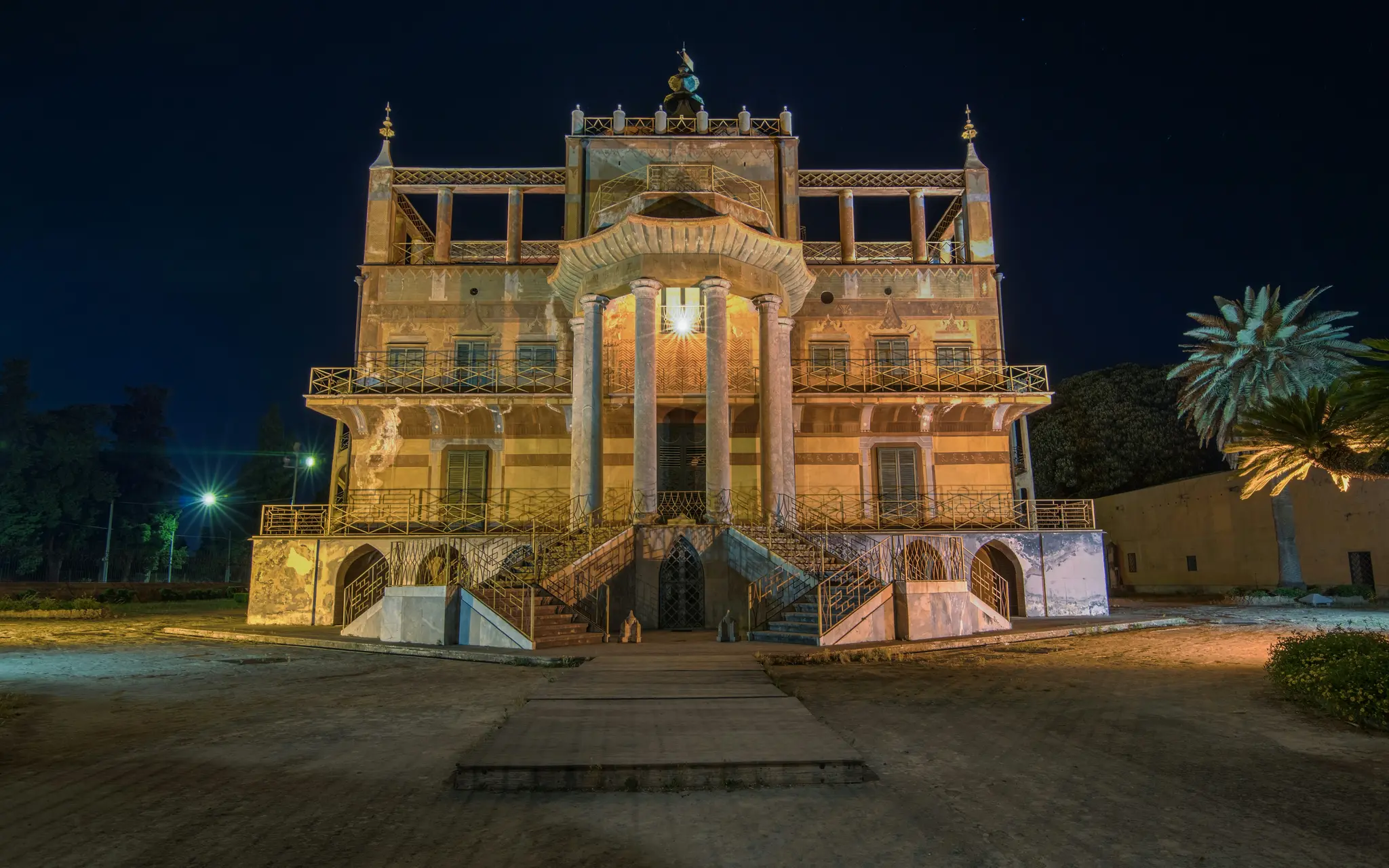 Un magnifico edificio a più piani con balconi e una scala centrale, brillantemente illuminato di notte su uno sfondo di cielo