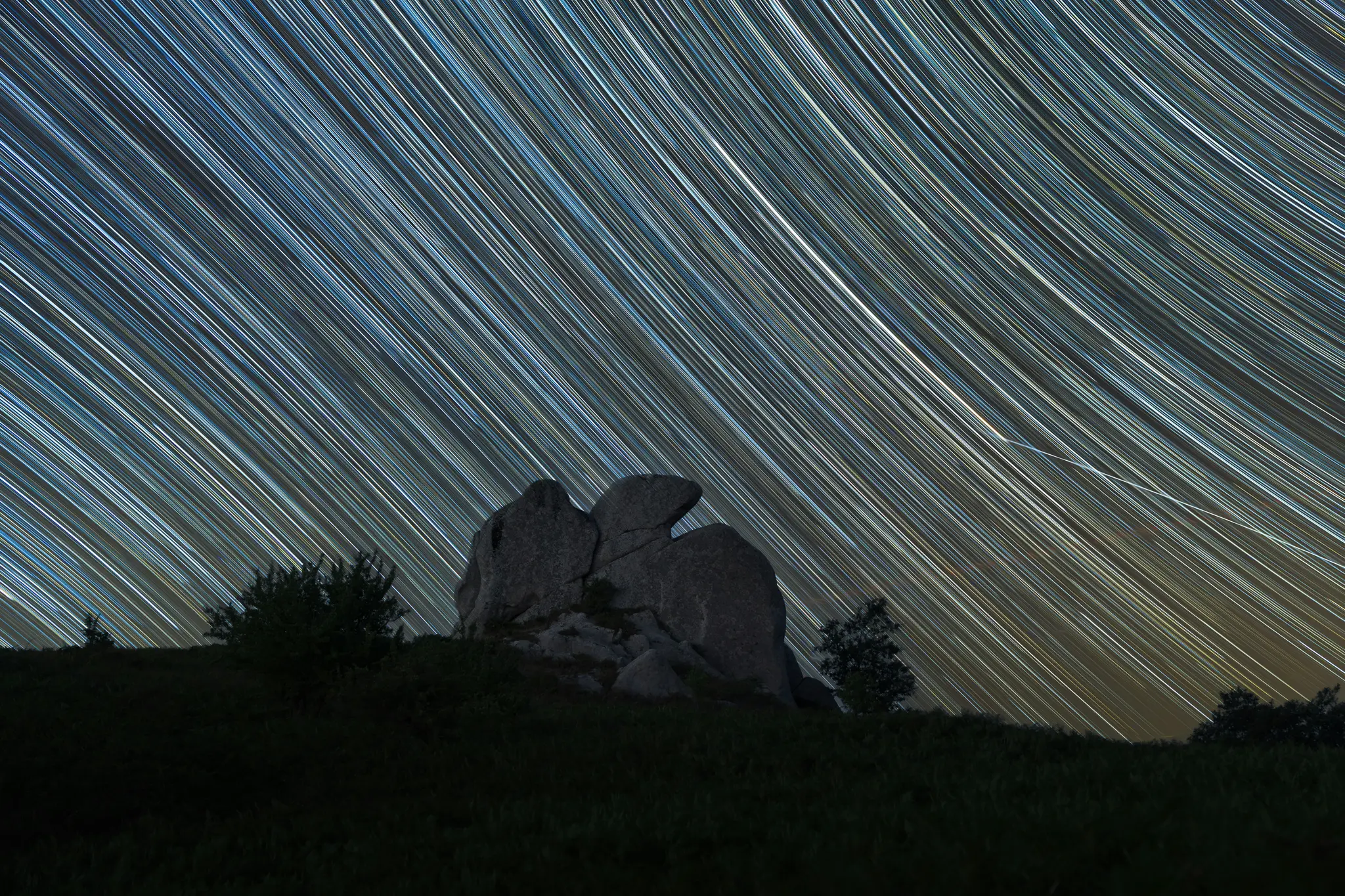 Una fotografía de larga exposición que muestra numerosas estelas de estrellas blancas y amarillas arqueándose sobre un cielo