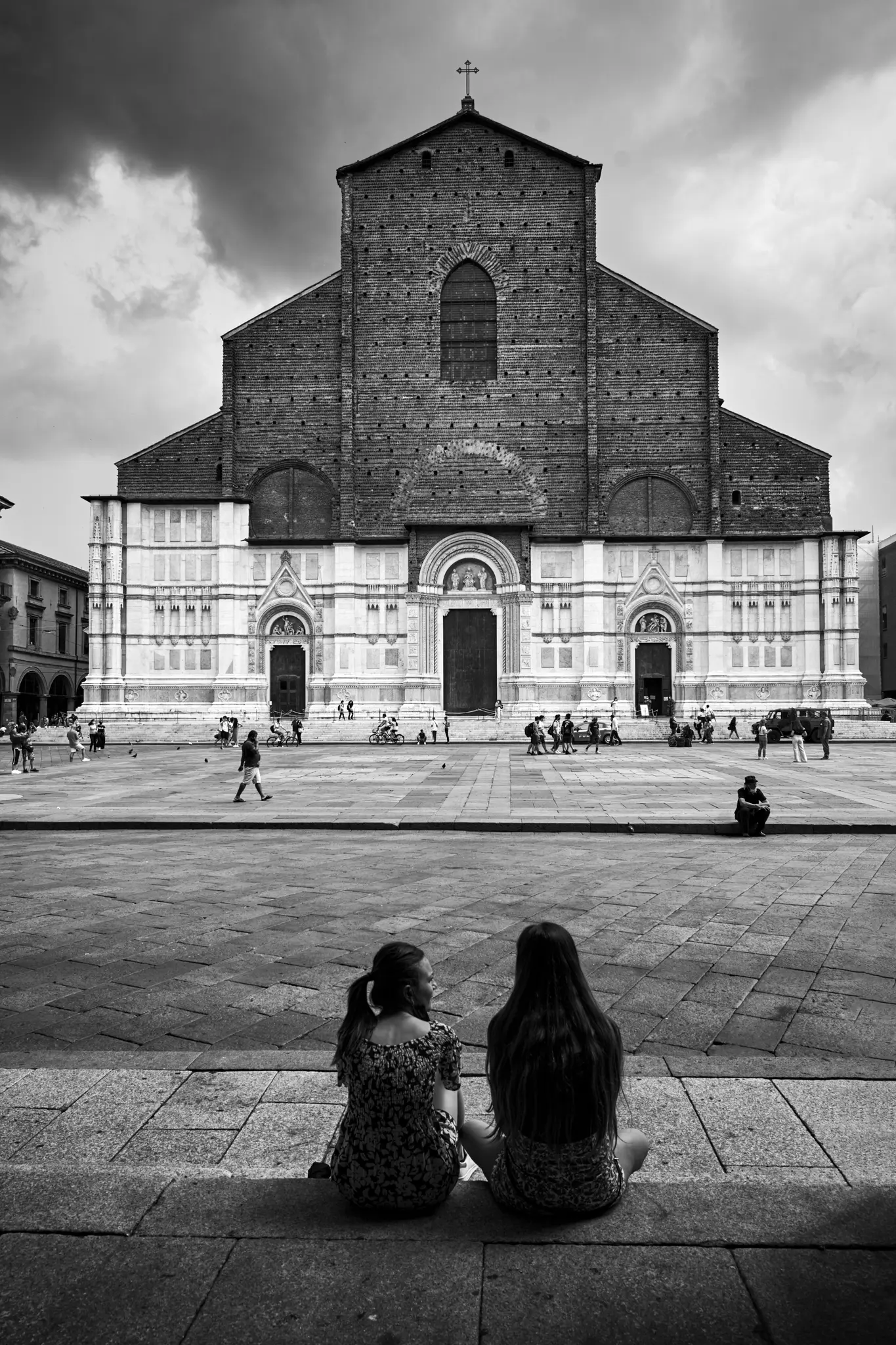 Photo en noir et blanc de deux femmes assises sur des marches, dos au spectateur, regardant une grande église de l'autre côté