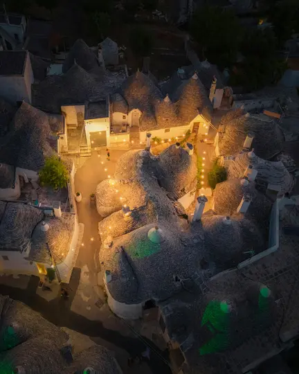 Et luftfoto om natten af en landsby med adskillige trulli-huse med koniske stentage, oplyst af varme lyskæder...