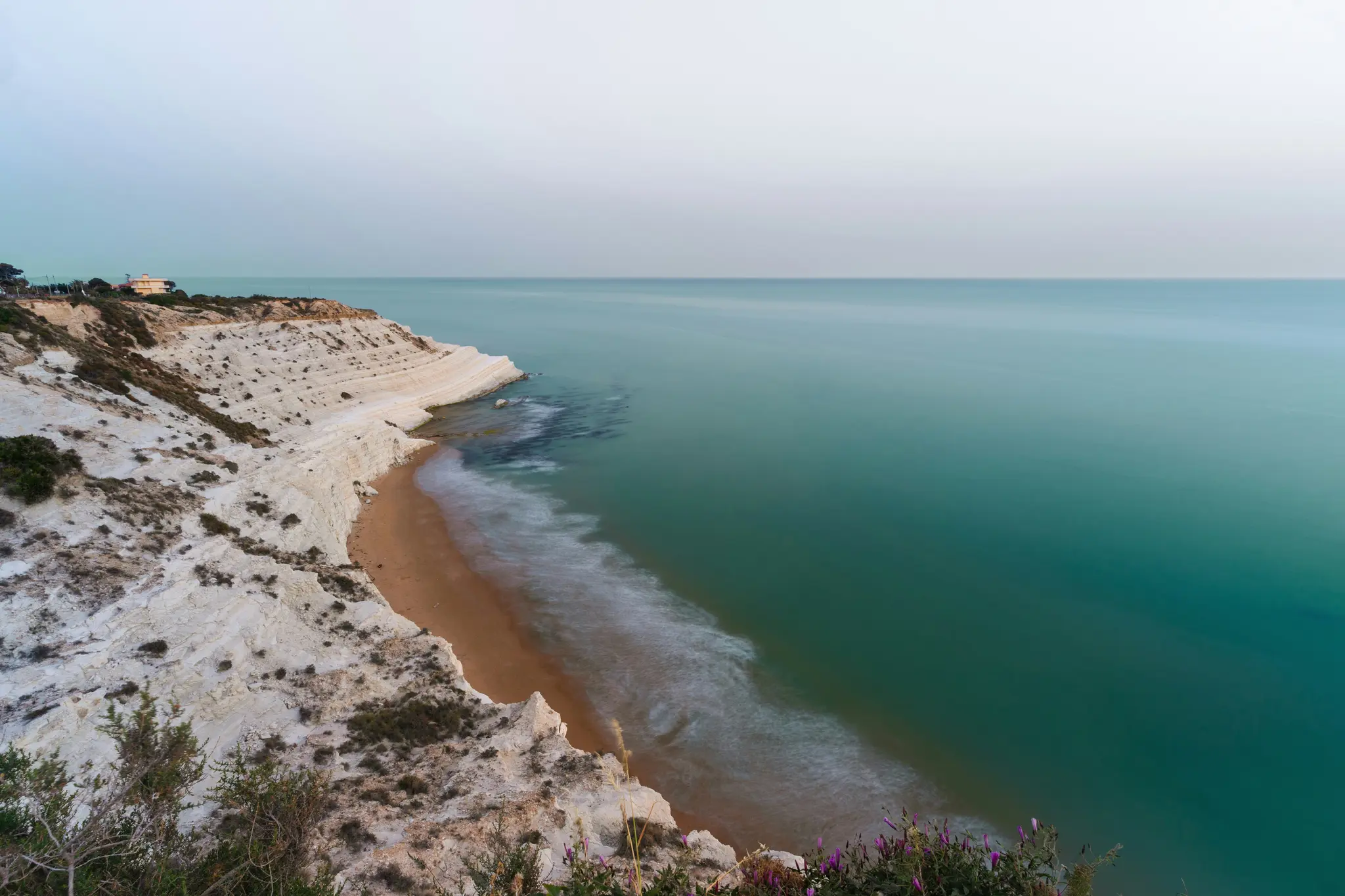 Una fotografia a lunga esposizione di una parete rocciosa bianca e stratificata che serpeggia lungo una spiaggia sabbiosa