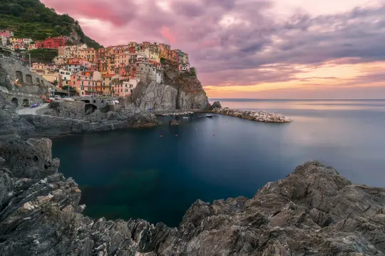 Et langtidsbillede af Manarola landsbyen i Cinque Terre, Italien, ved solnedgang. Farverige huse klamrer sig til en klippe…