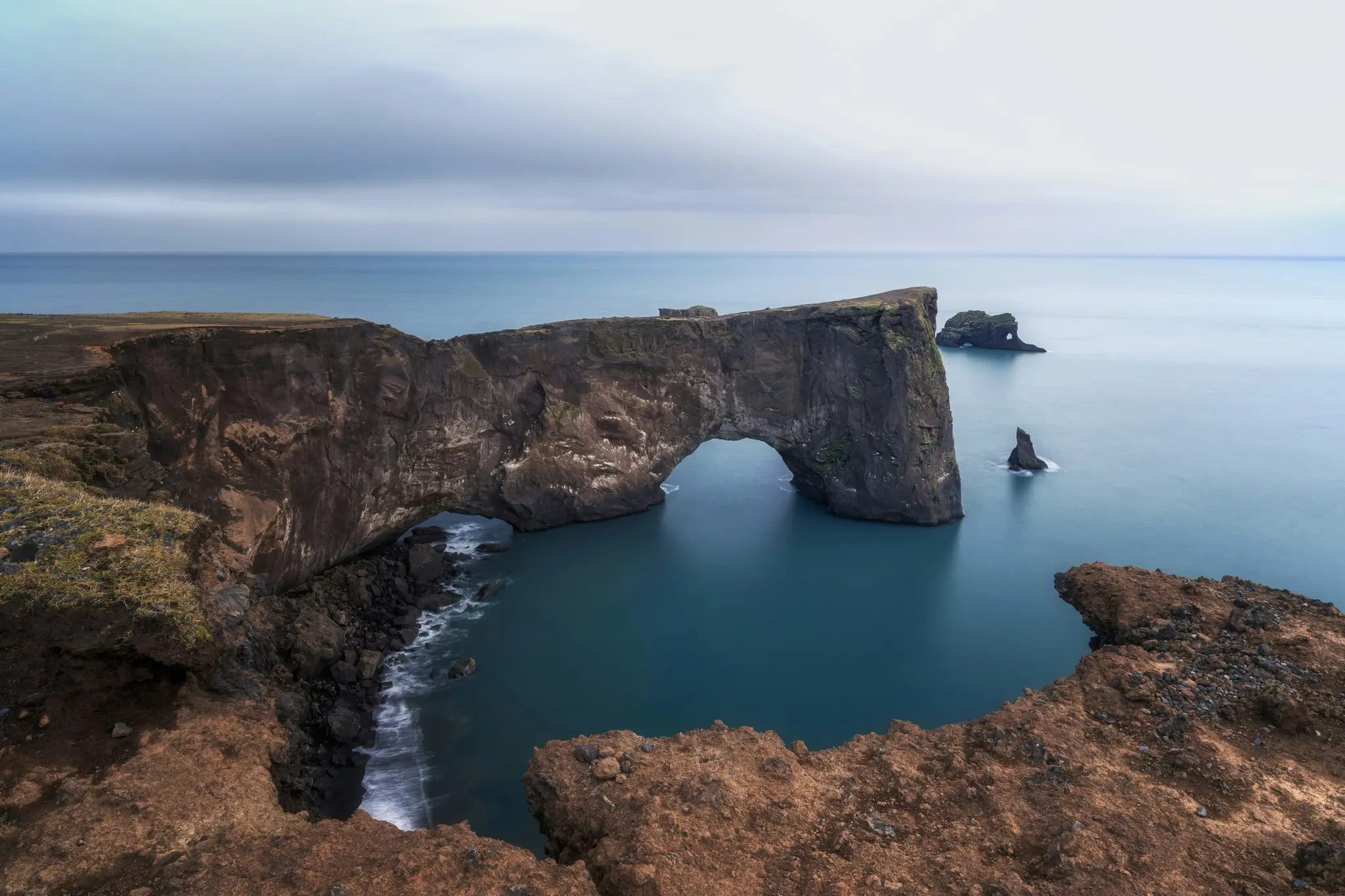Un'ampia vista panoramica dell'arco roccioso di Dyrhólaey in Islanda, che si estende in un mare blu calmo sotto un cielo