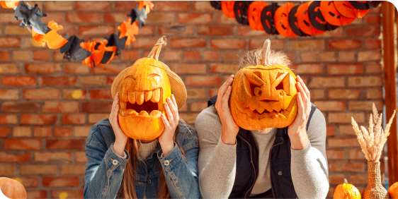 Two people holding carved pumpkins in front of their faces