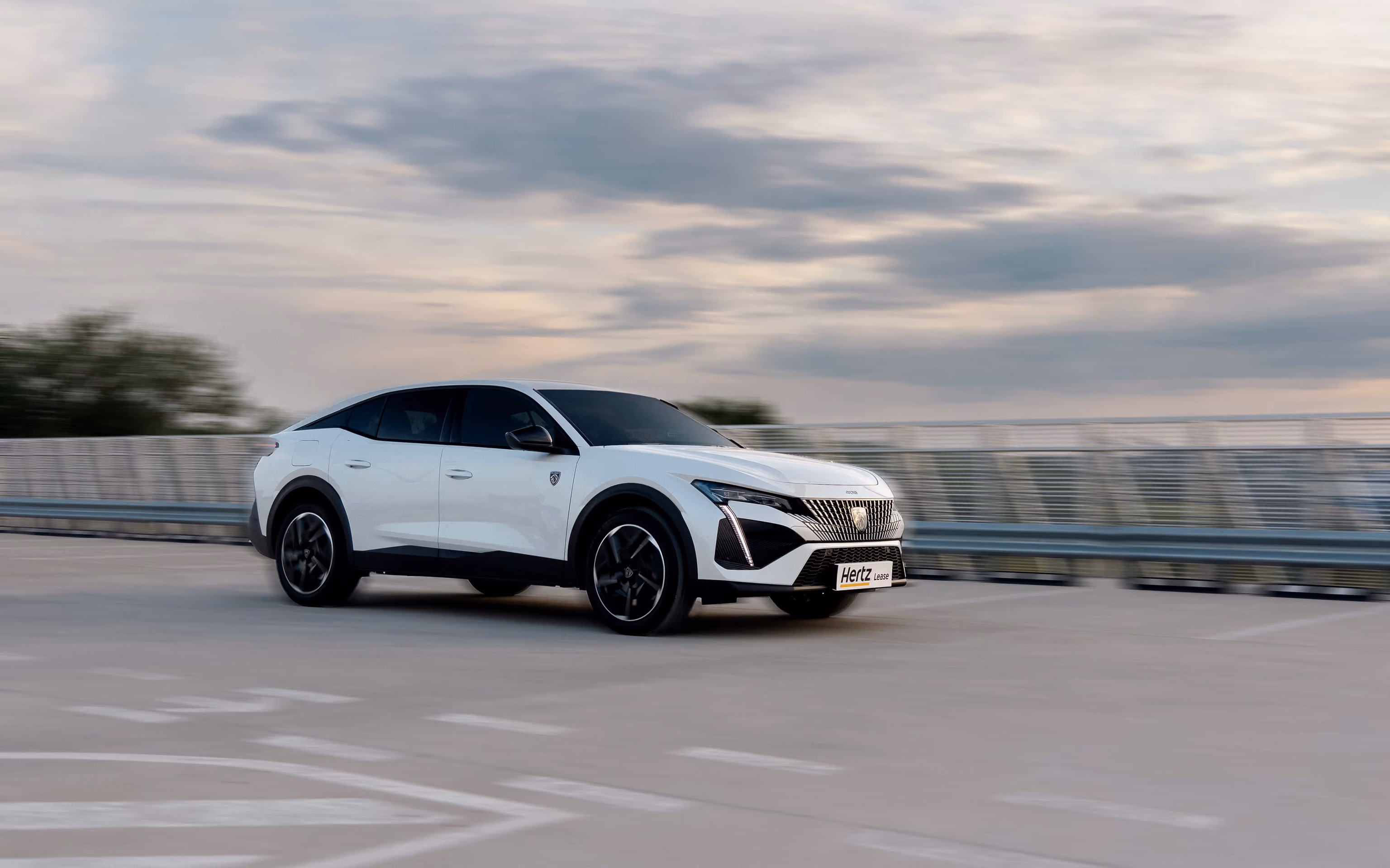 White SUV in motion on an overpass, cloudy sky and motion blur - a Hertz Lease brand photo.