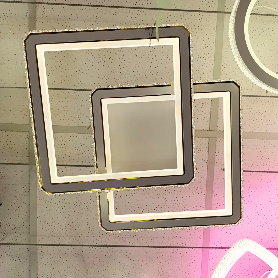 Сучасна квадратна світлодіодна люстра білого кольору з декоративною каймою з кристалів, стильний мінімалістичний дизайн, два пересічних світлових квадрати, фото з виставки освітлення, світильник для вітальні, кухні або спальні, інтер’єр магазину, відбиття світла на глянцевій поверхні стелі, акцент на тренди освітлення 2025 року