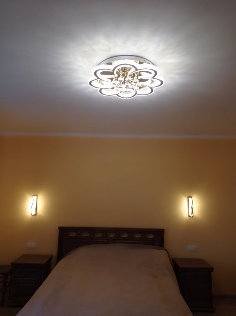 світлодіодна люстра з кристалами золото на стелі в спальні клієнта, встановлена ​​над ліжком, створює м'яке біле освітлення з розсіяними тінями, фотовідгук з реального інтер'єру, площа близько 15 м², стиль — сучасний класика, два настінні світильники з боків