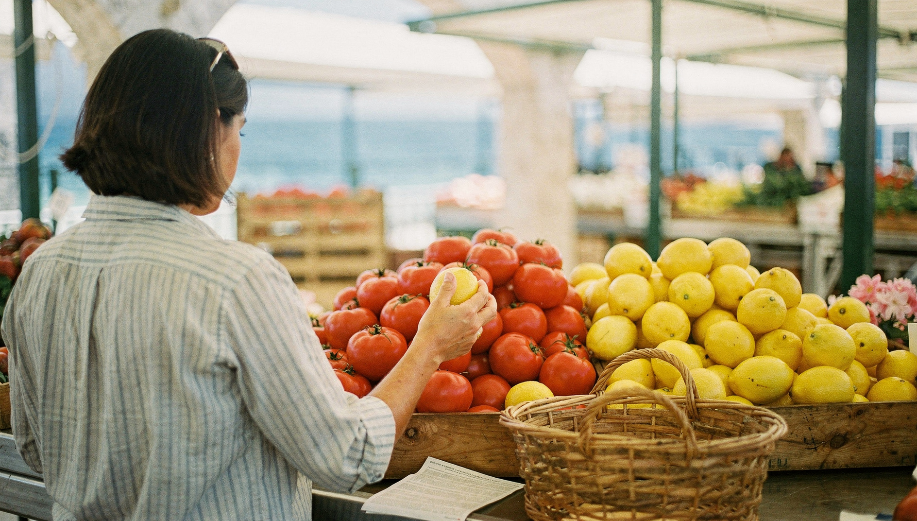 En kunde i stripete skjorte velger sitroner ved en overbygd markedsbod i Dénia