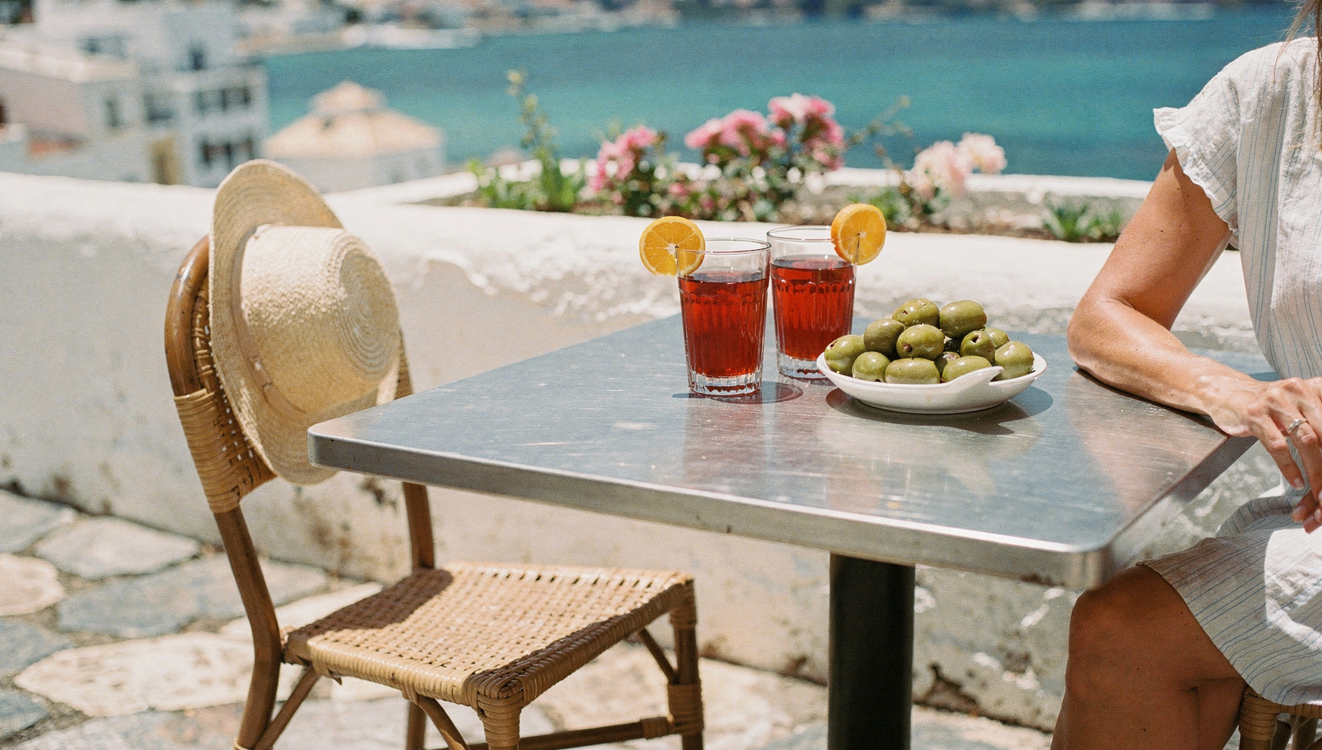 Vermouth and olives on a café table with a straw hat on a wicker chair