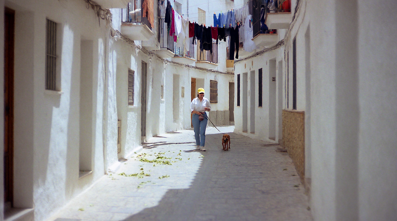 A woman and her dog walking through a whitewashed old town street
