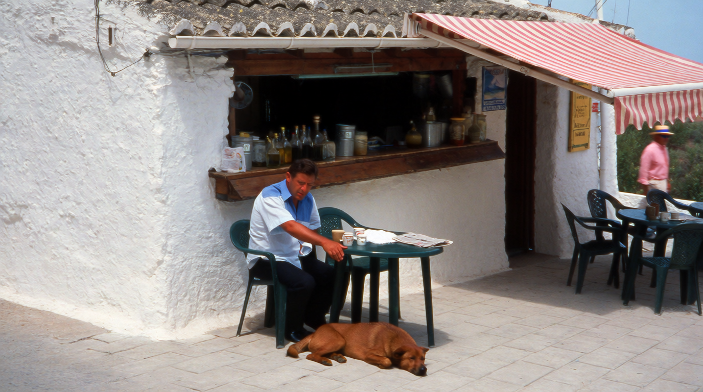 A dog resting under a café table on a village terrace