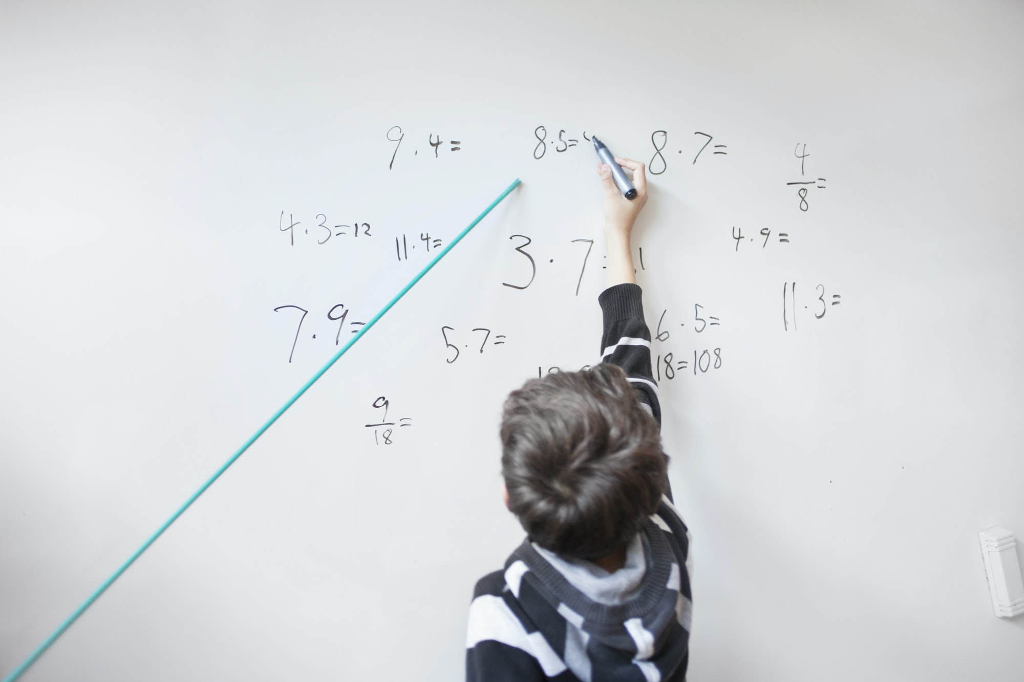 Rear view of boy writing on whiteboard in classroom