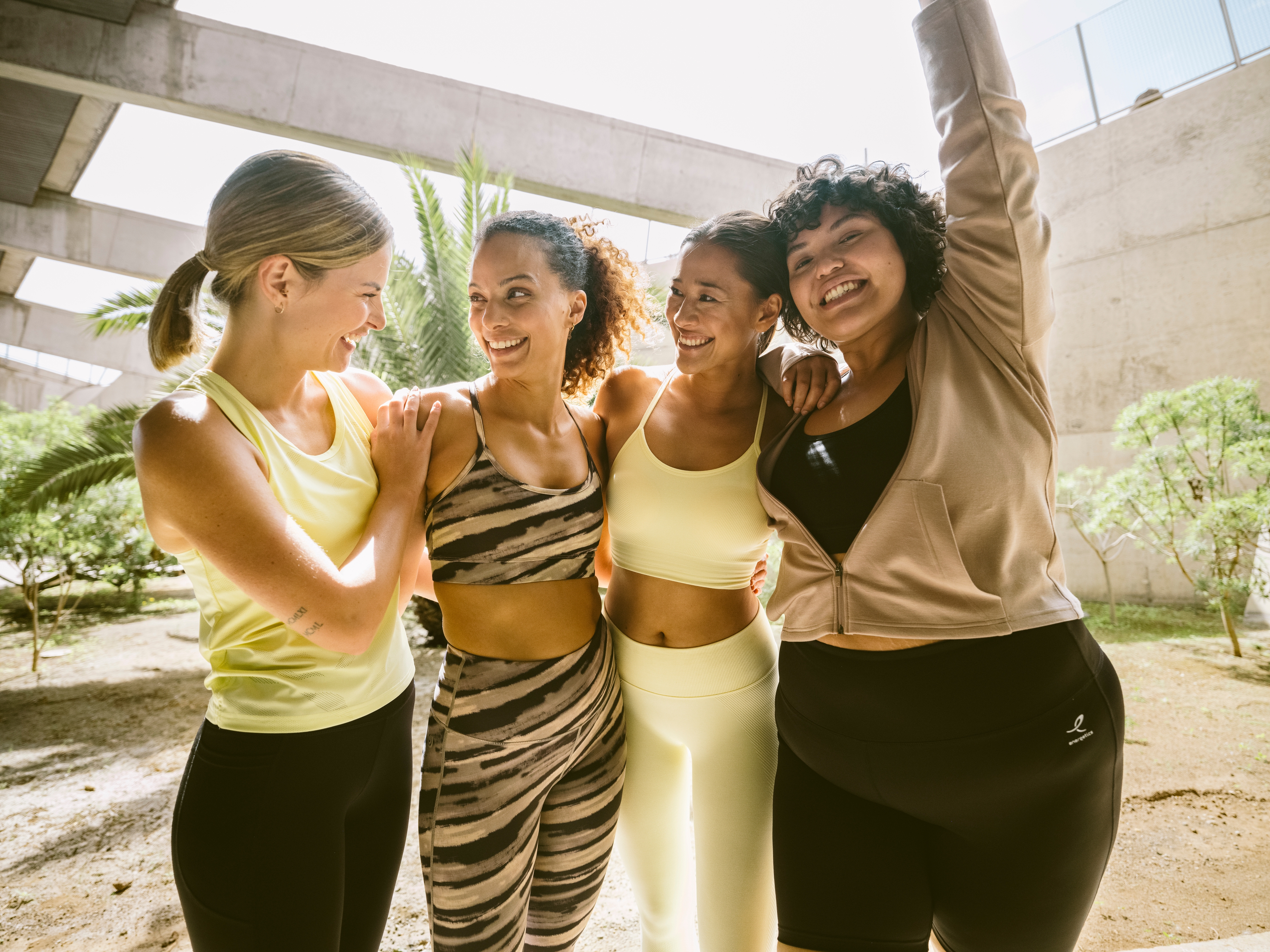 Lächelnde Frauengruppe, die sich in den Armen hält und moderne Sportkleidung trägt 