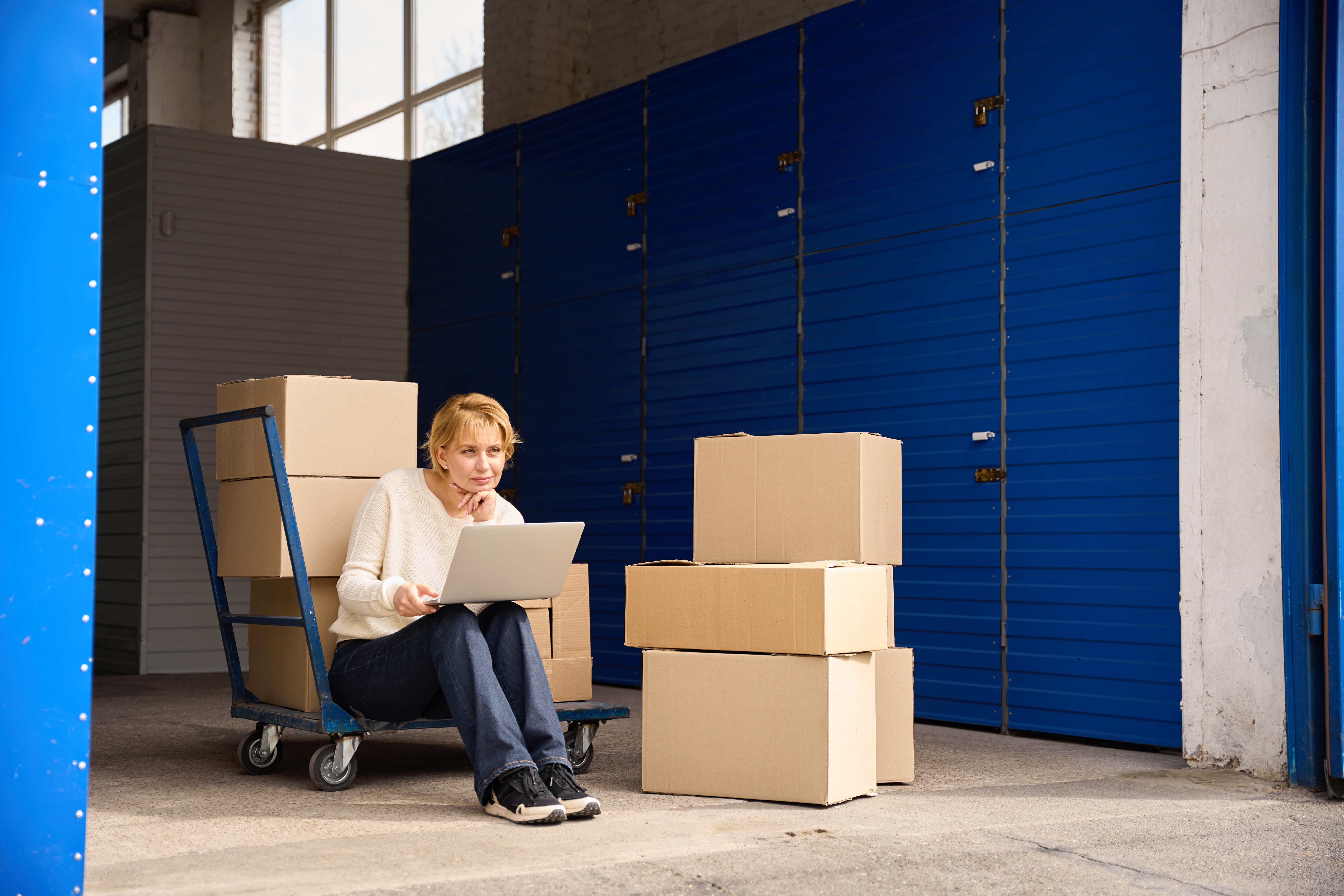 Person with a laptop surrounded by boxes in a storage facility