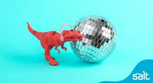A plastic t-rex with noise cancelling headphones on in front of a disco ball to showcase the need to attract and retain autistic talent