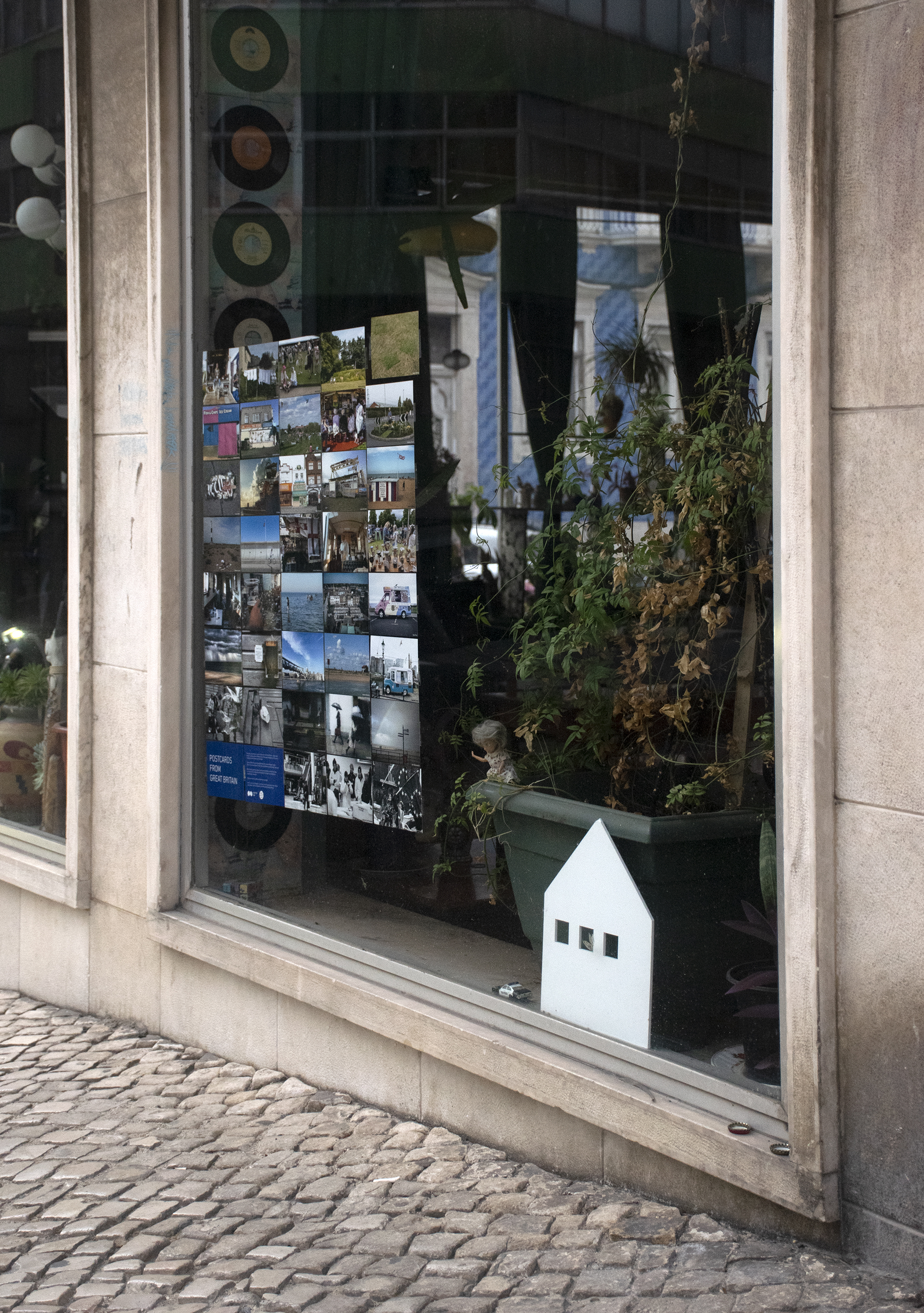 A street in Lisbon, Portugal. In one of the shop windows there is an exhibition of Shutter Hubs Postcards from Great Britain project, lots of postcard sized photographs