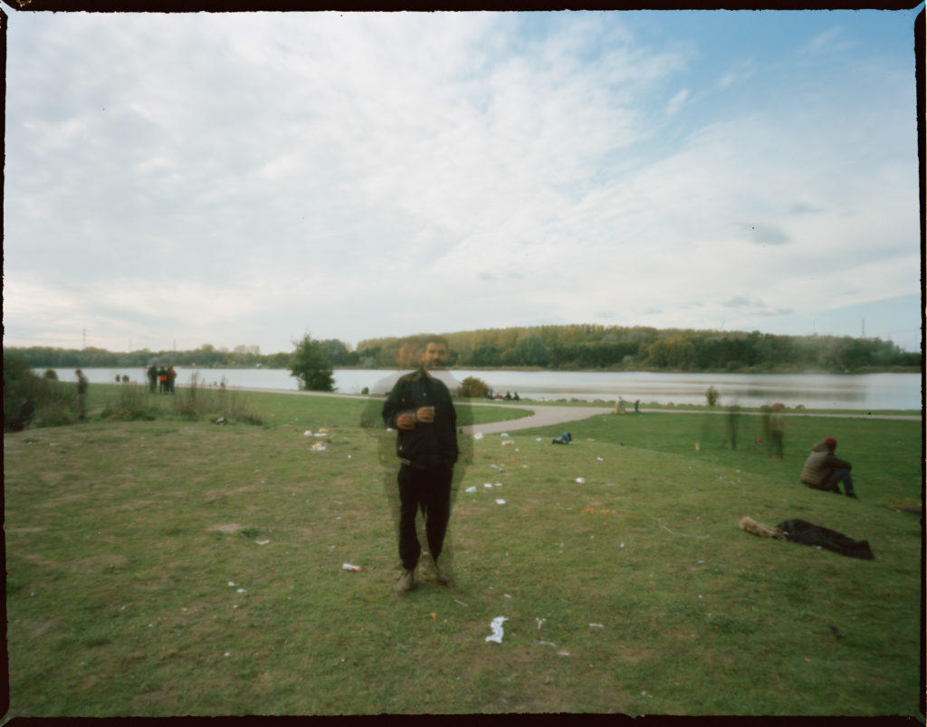 A refugee who is out of focus photographed with a campsite's lake in the background.
