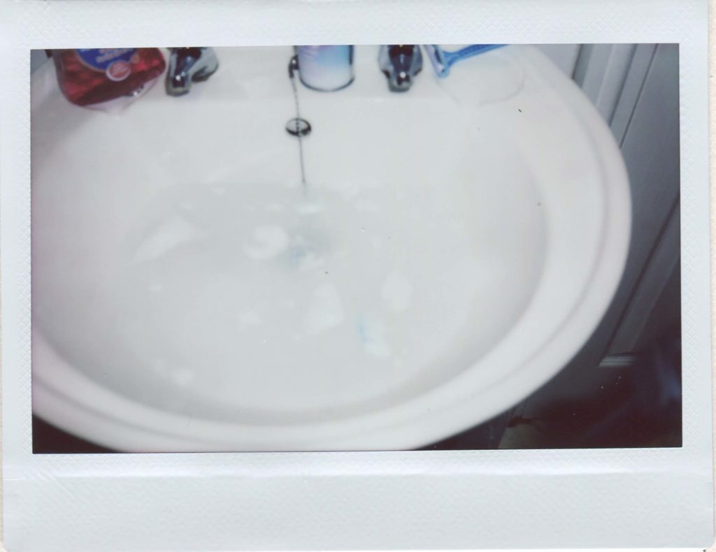 Instax wide print of a bathroom sink. it is half-filled with water, and there's clumps of shaving foam floating on the top