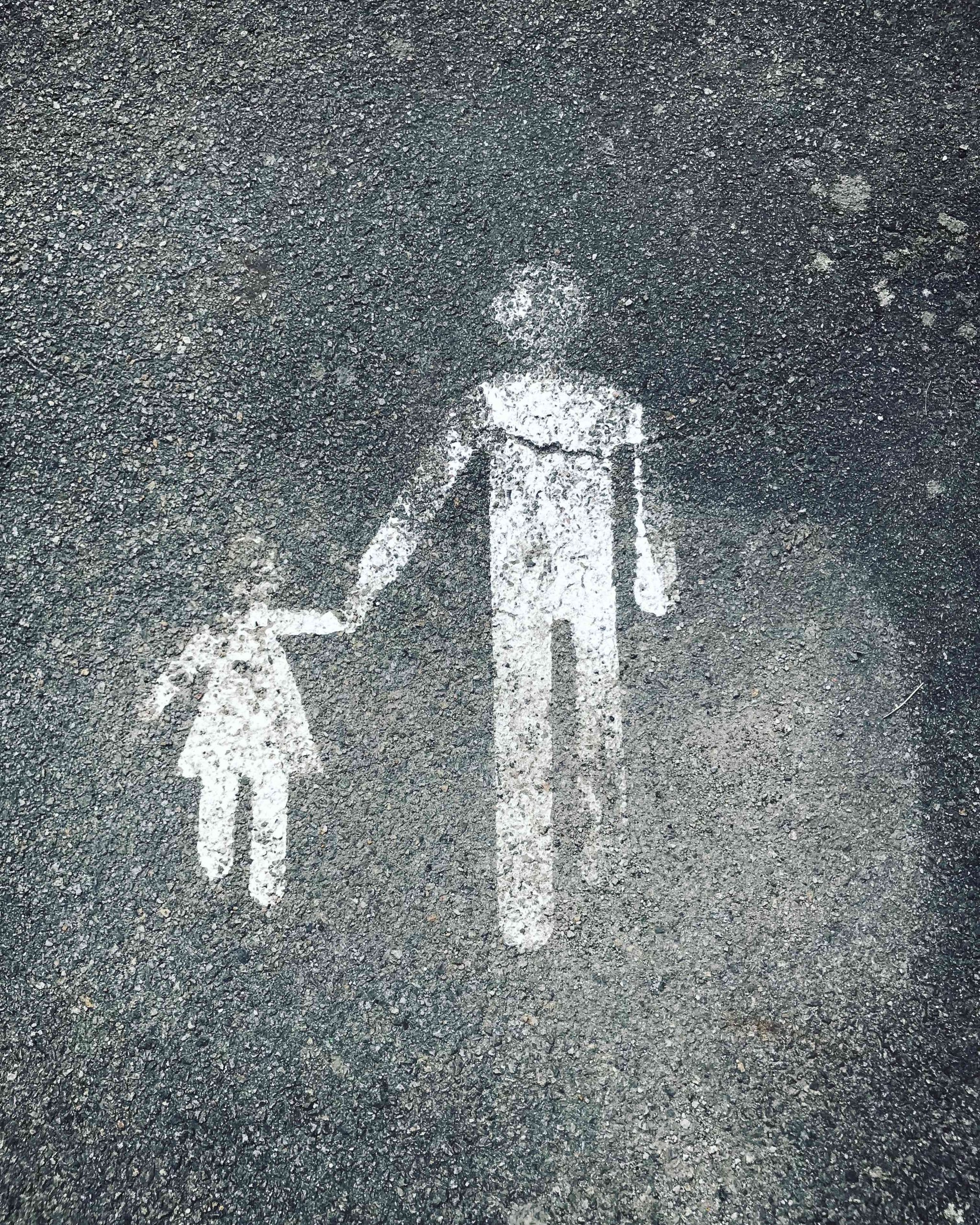 Photograph of a floor surface painted with a white graphic of a small person in a dress holding hands with a taller person in trousers