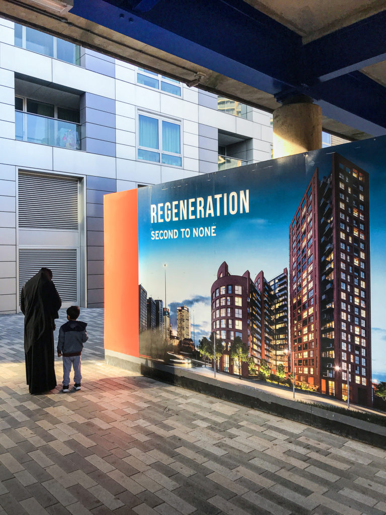 Photograph of mother and child next to luxury development hoarding saying regeneration second to none.