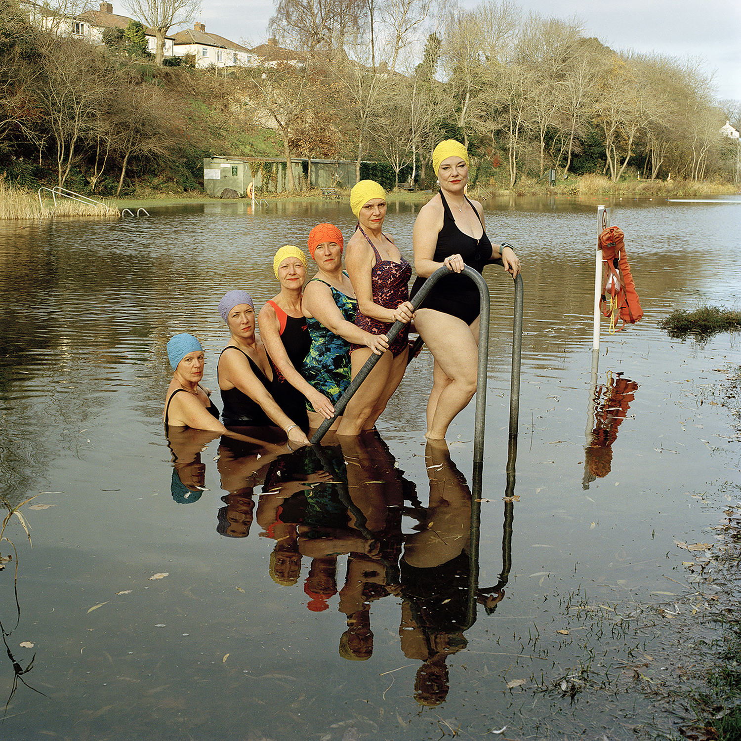 6 swimmers stood on a ladder in a lake with reflection