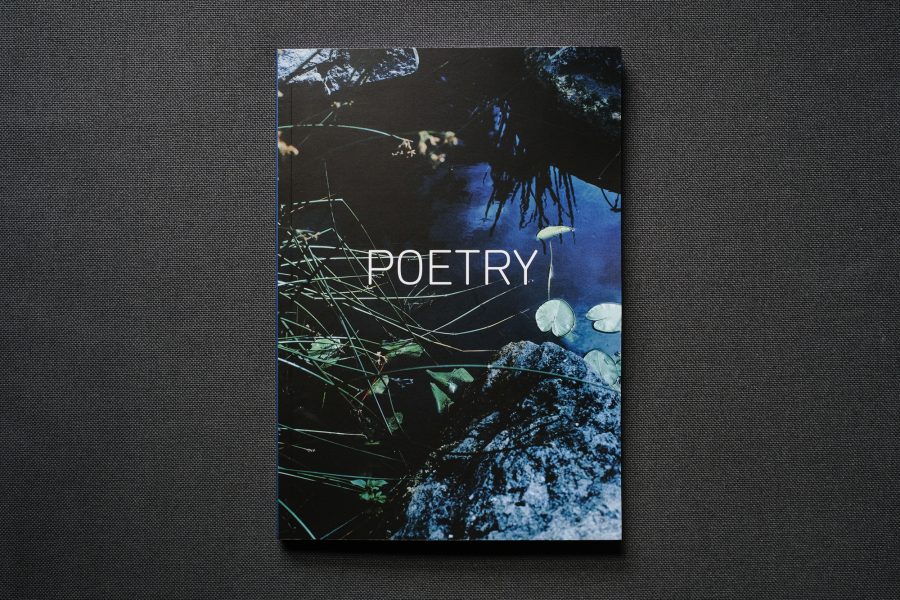 Photograph of a book on a dark grey background. The book cover shows a body of water with plant life, shadows and reflections and the word 'POETRY' in white in the centre