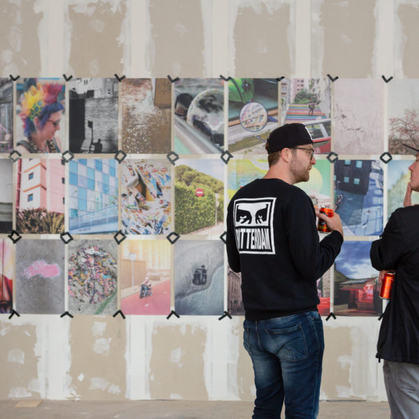 Two people having a discussion in front of the Shutter Hub STREET / FORM exhibition at POW! WOW! Rotterdam, showing a wall in an empty shop premises with newsprint images taped to the wall