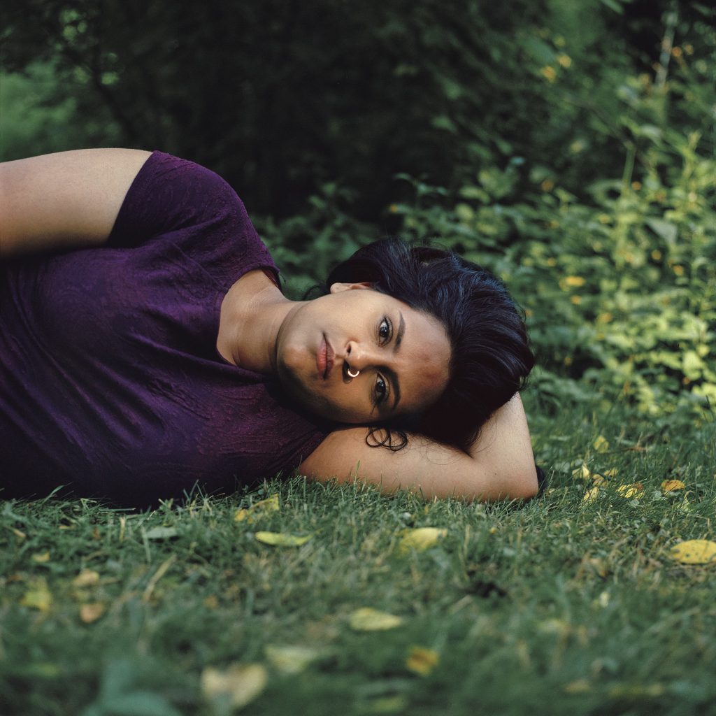 Photographic portrait of reclining woman, on grass, with dark hair and dark purple dress
