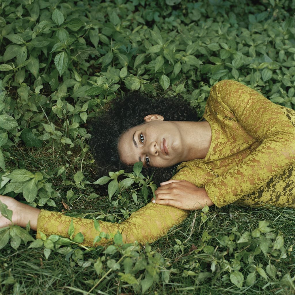 Photographic portrait of reclining women, on green grass, with dark hair and yellow blouse