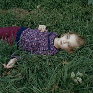 Photographic portrait of reclining girl on green grass, with purple blouse and pants