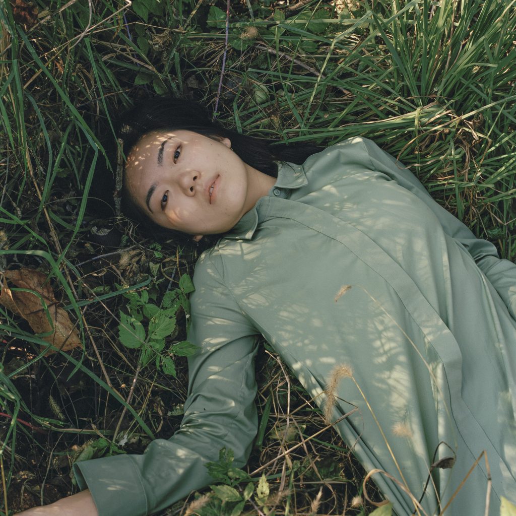 Photographic portrait of reclining woman on green grass, with dark hair and green blouse